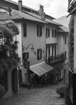 Black and white view of a quaint European street with cobblestone and buildings in the rain.