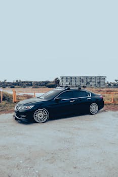 Sleek luxury sedan parked on a rural gravel road with clear sky backdrop.