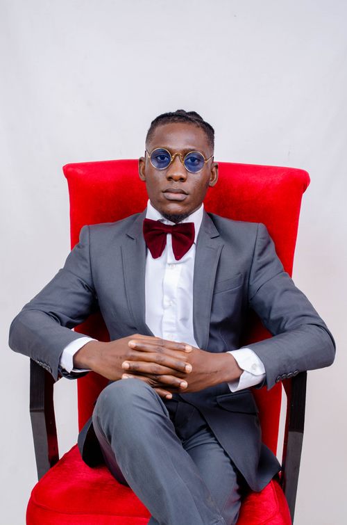 Free Elegant portrait of a man in a gray suit sitting confidently on a red chair, exuding fashion and style. Stock Photo