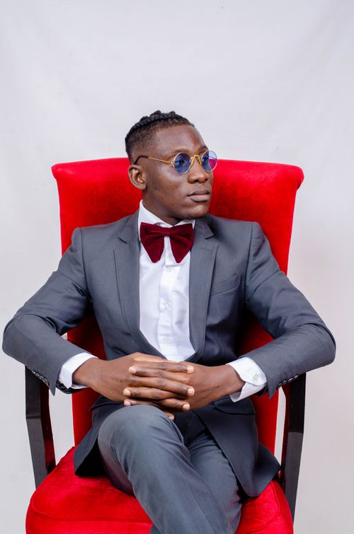 Free Portrait of a man in a gray suit and sunglasses seated against a red armchair. Stock Photo