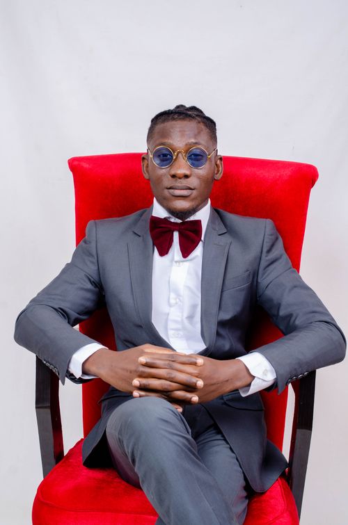 Free Fashionable portrait of a man in gray suit sitting in red armchair with sunglasses and bow tie. Stock Photo