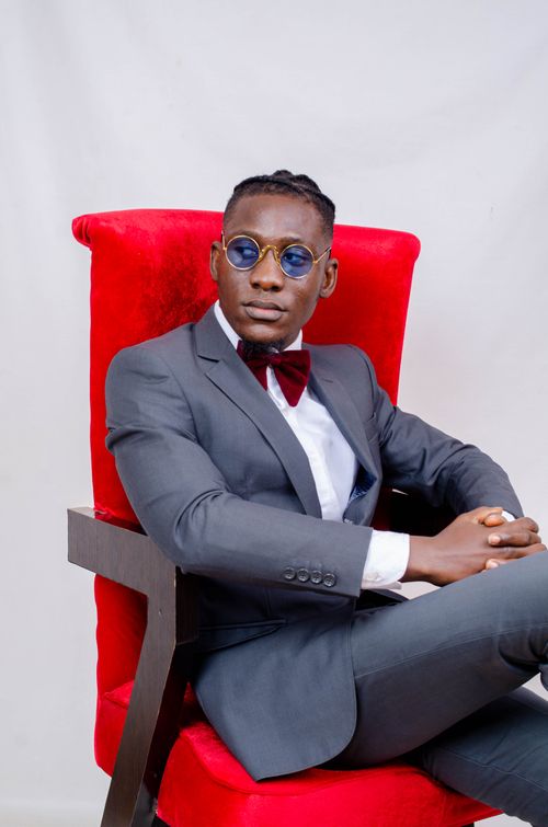 Free Sophisticated portrait of a stylish man in a gray suit and bow tie seated on a red armchair with a white background. Stock Photo