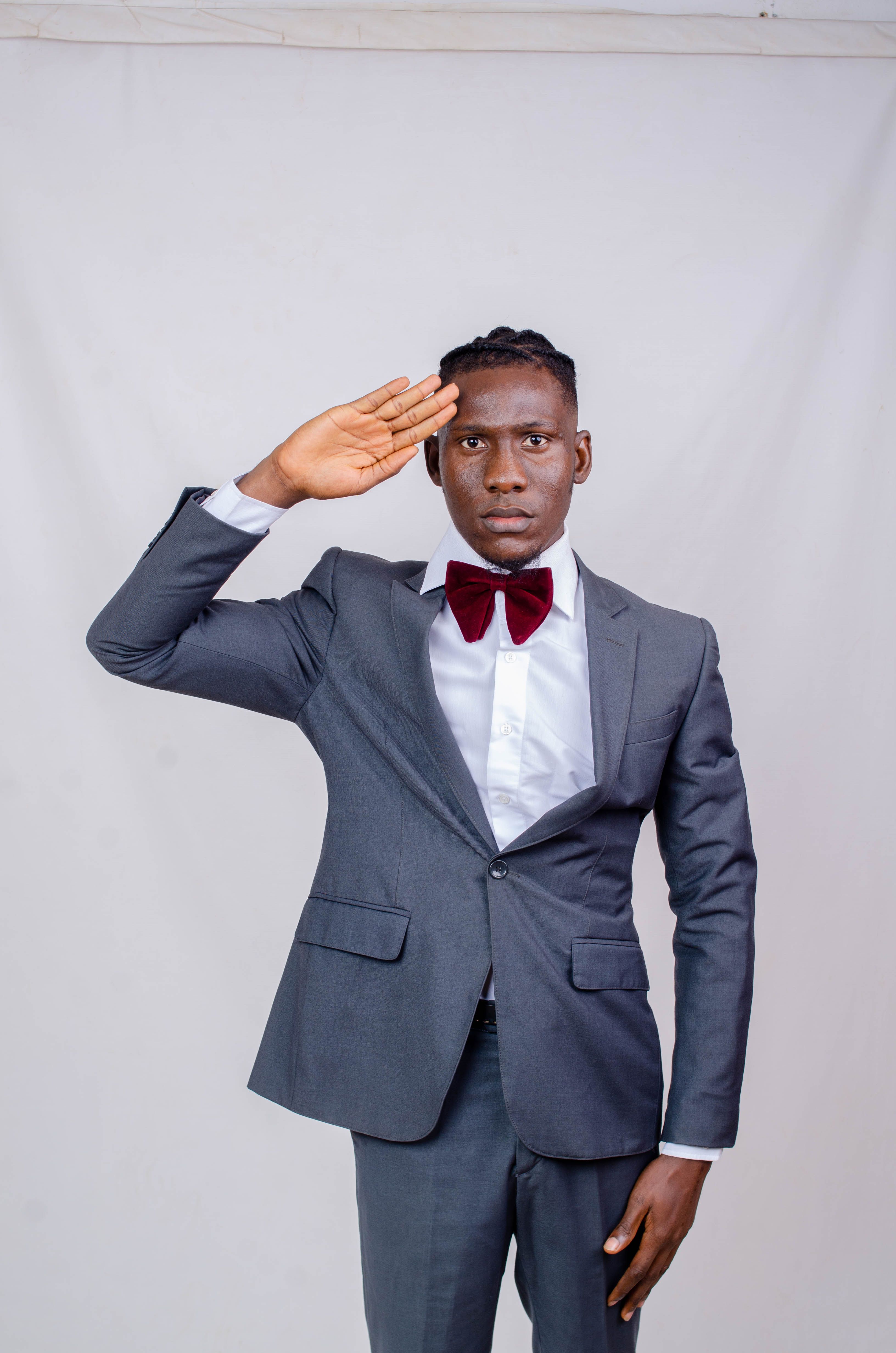 Young Black man in formal attire saluting against a studio backdrop, showcasing elegance and professionalism.