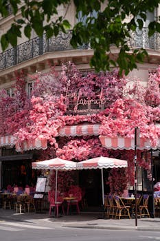 Vibrant Parisian cafe adorned with pink blossoms, offering outdoor seating and a charming urban vibe.