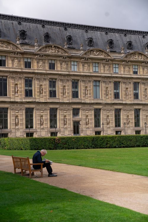 Free A solitary man reads on a bench outside the historic Louvre Palace in Paris. Stock Photo