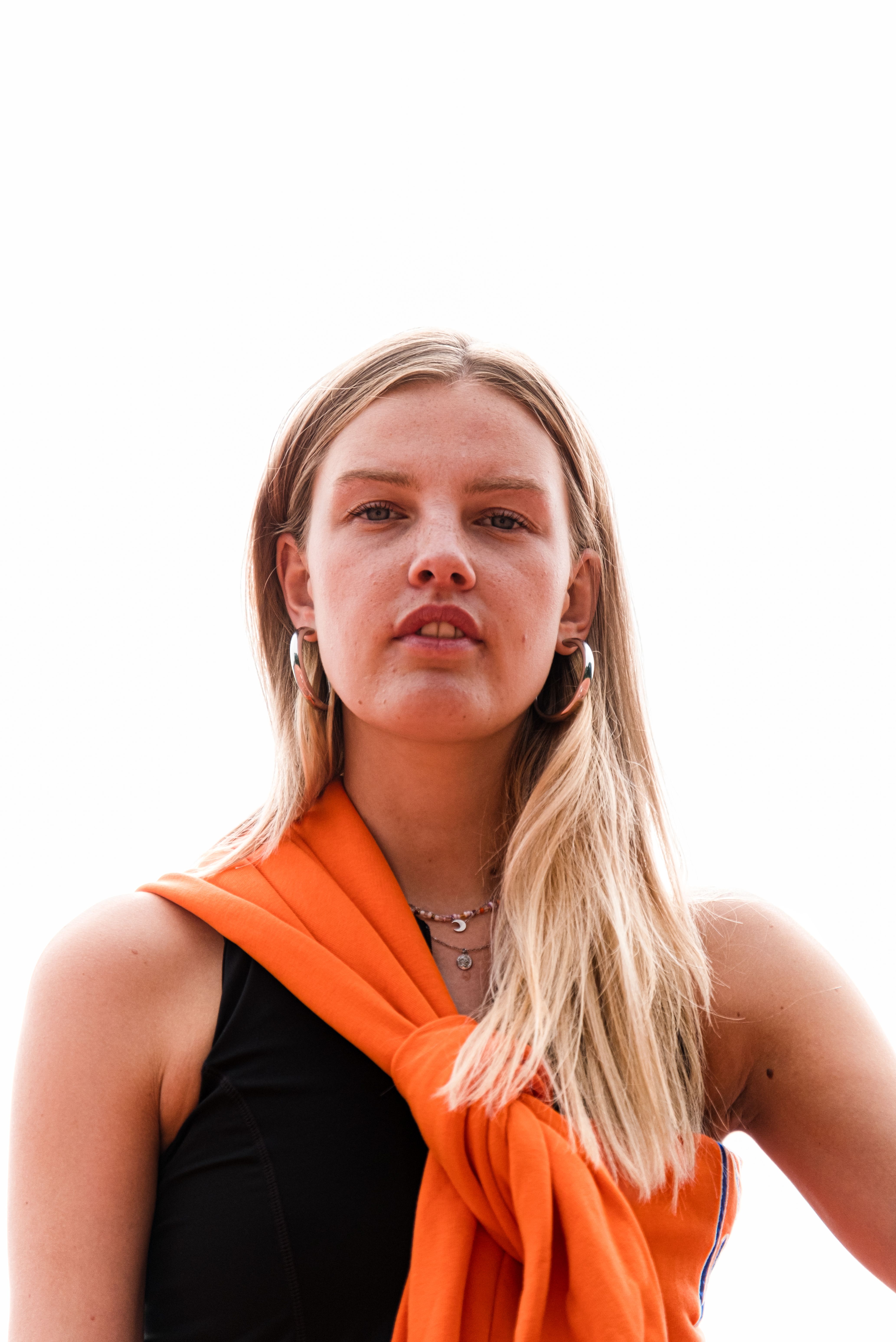 Stylish blonde woman posing in bright fashion with orange scarf and earrings.