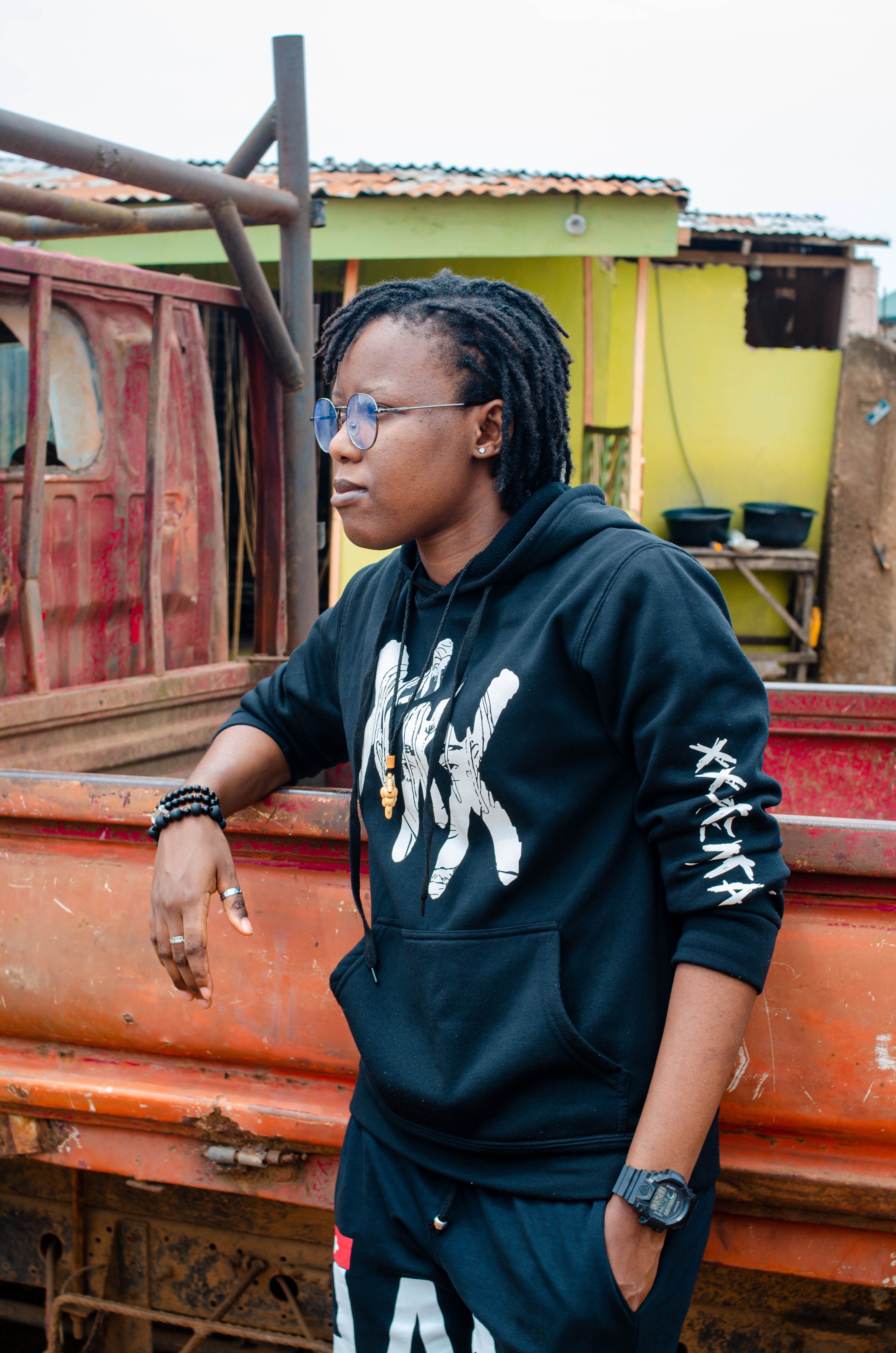 Stylish woman in a black hoodie standing outdoors with a rustic backdrop.
