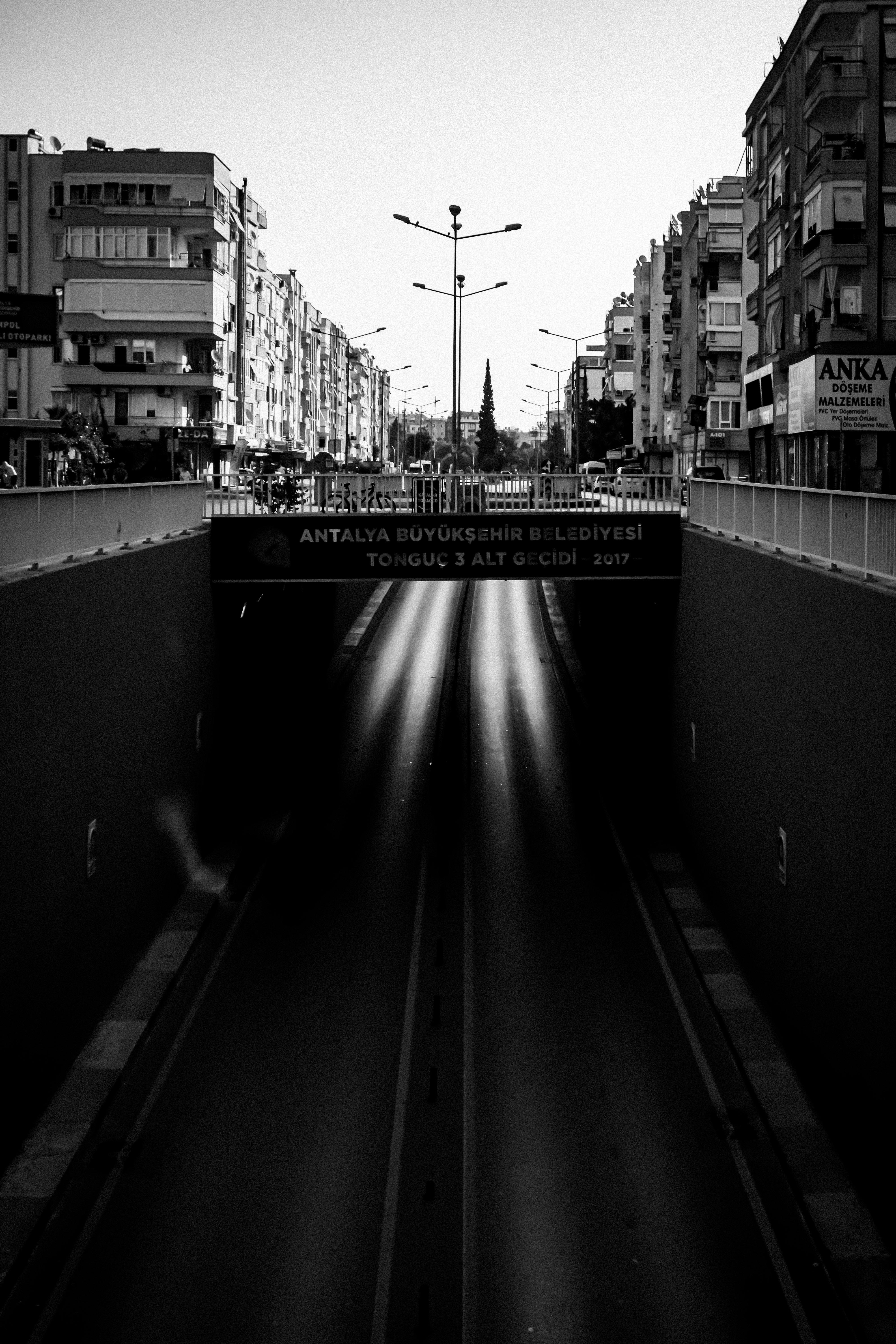 Black and white photo of an empty urban tunnel in a city street under a bridge.