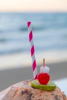 Vibrant tropical drink with fruit and straw by the beach, perfect for summer enjoyment.