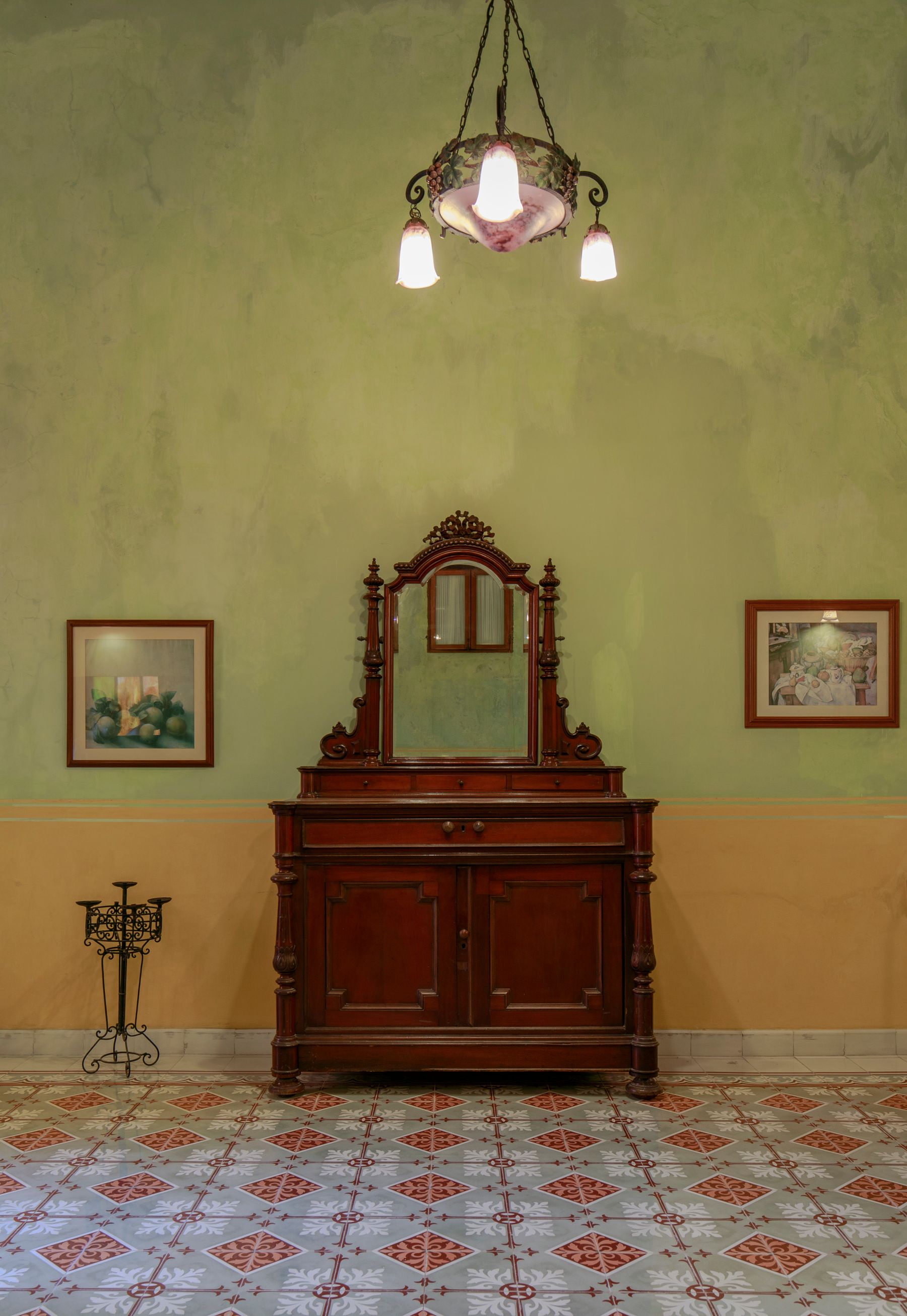 Timber cabinet and tall framed mirror beneath a decorative pendant on a green-and-ochre wall