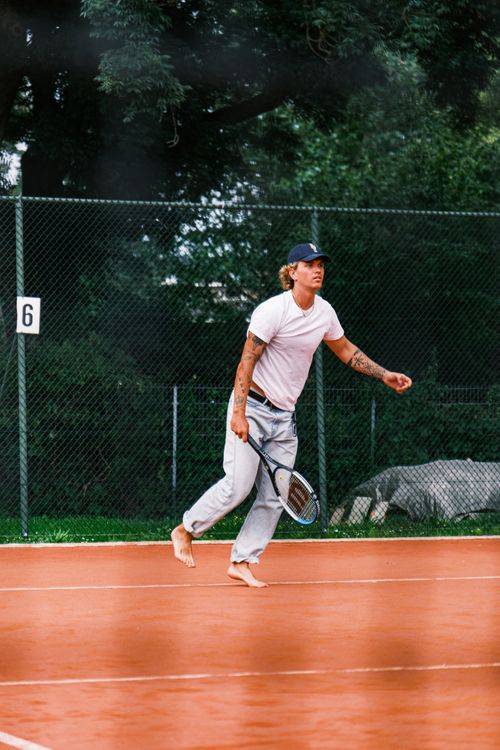 Free A tennis player skillfully maneuvers barefoot on a clay court during a vibrant day outdoors. Stock Photo
