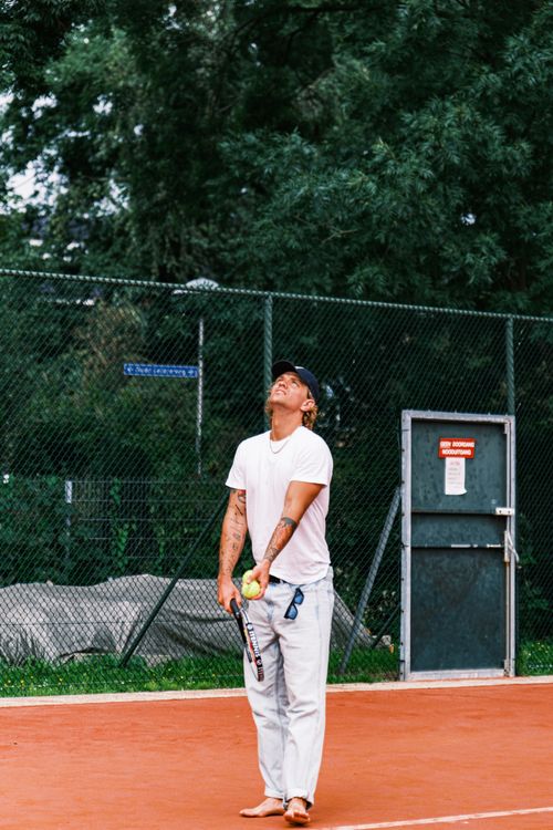 Free Man preparing a tennis serve barefoot on a clay court with a scenic outdoor background. Stock Photo