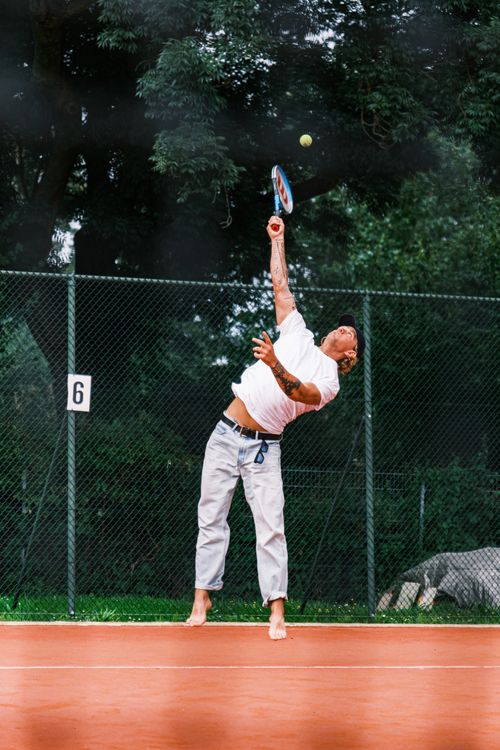 Free Adult man serving a tennis ball barefoot on an outdoor court during daylight. Stock Photo