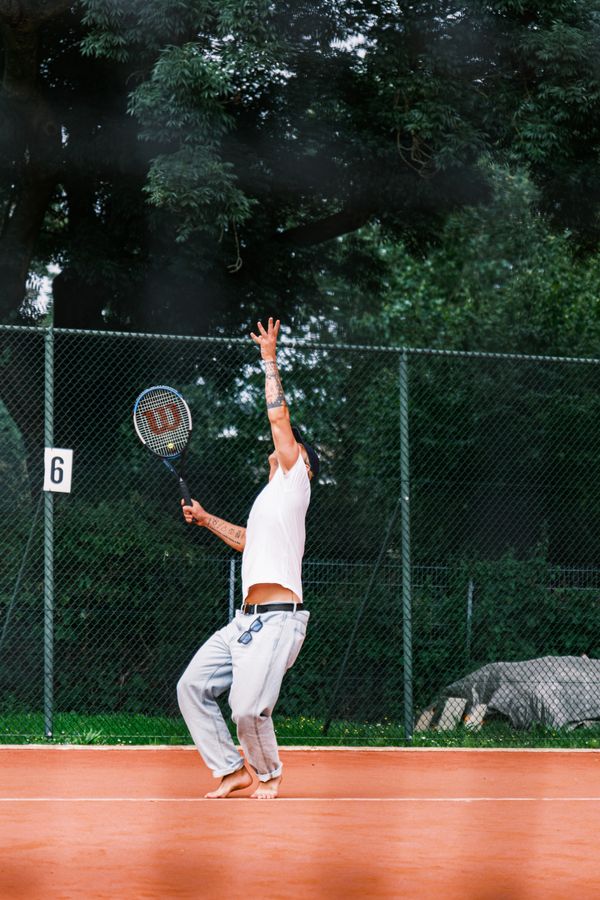 Player serving on a clay court under the trees