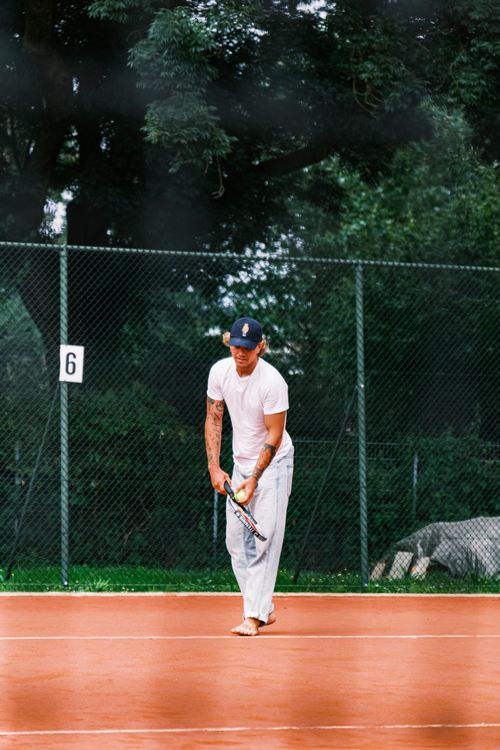 Free A man in casual attire is serving on a clay tennis court, creating a casual sports atmosphere. Stock Photo
