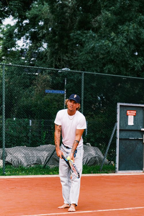 Free Man playing tennis barefoot on a clay court, ready to serve a shot. Stock Photo