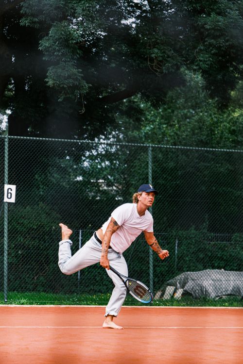 Free Dynamic shot of a barefoot man playing tennis on an outdoor clay court surrounded by greenery. Stock Photo