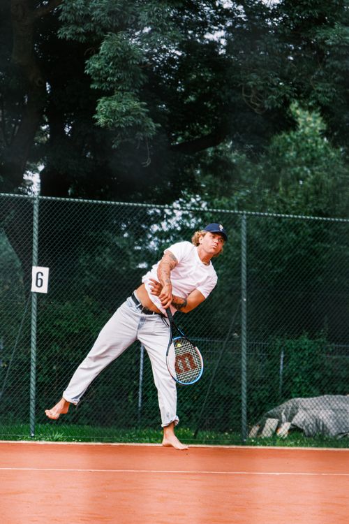 Free Male tennis player serving barefoot on an outdoor court, showing action and focus. Stock Photo