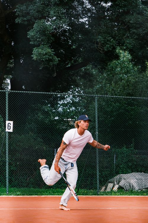 Free Dynamic shot of a barefoot man playing tennis outdoors on a clay court in daylight. Stock Photo