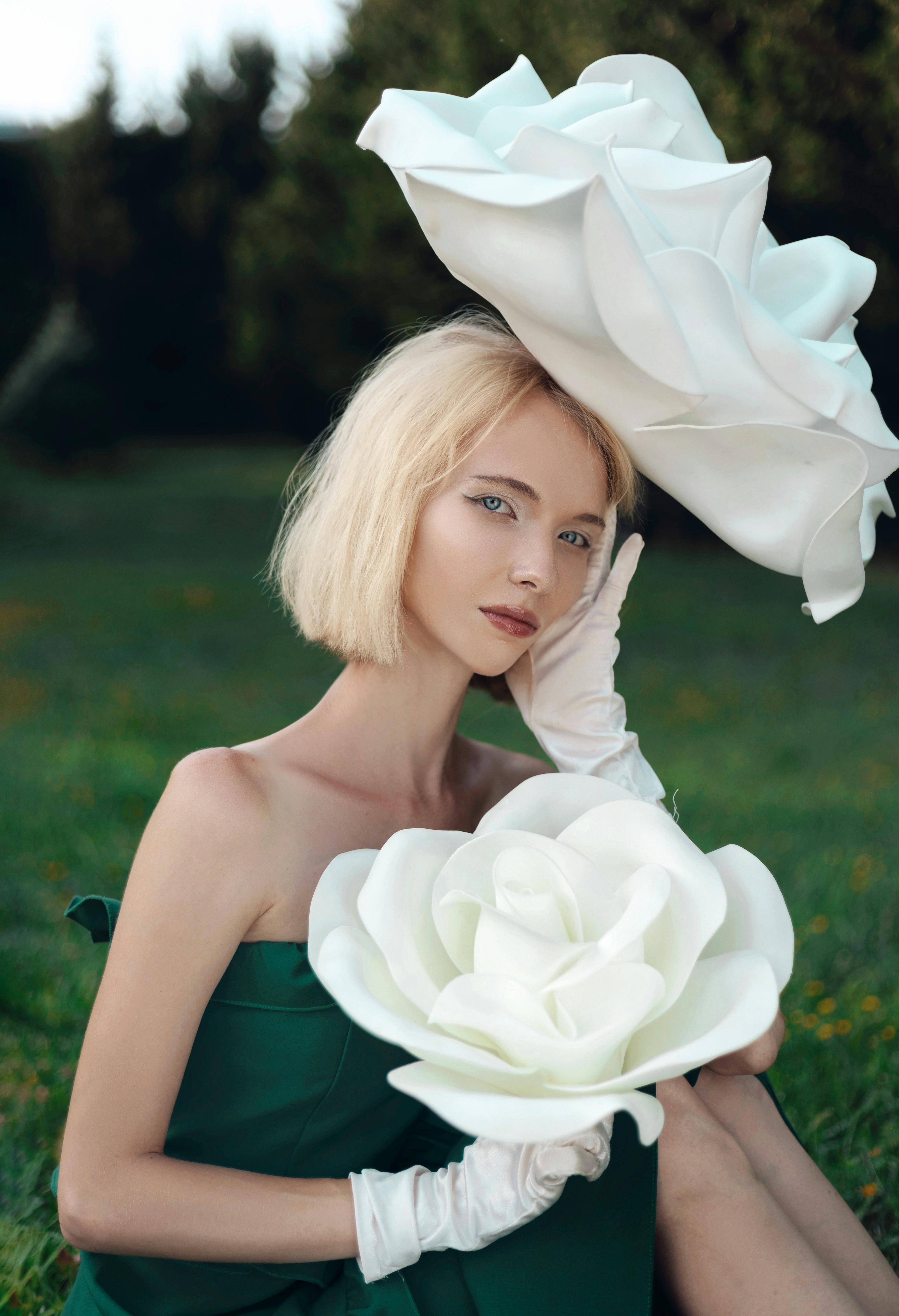 A fashion-forward woman in a green dress, posing with oversized white flowers, creates a chic outdoor portrait.