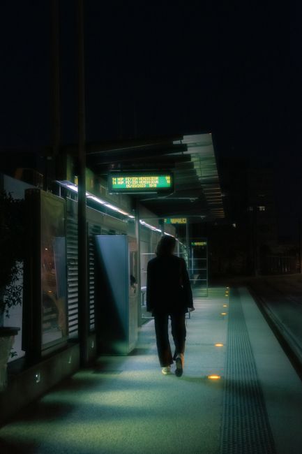 Silhouetted figure walking at night in an urban station, under artificial lights.