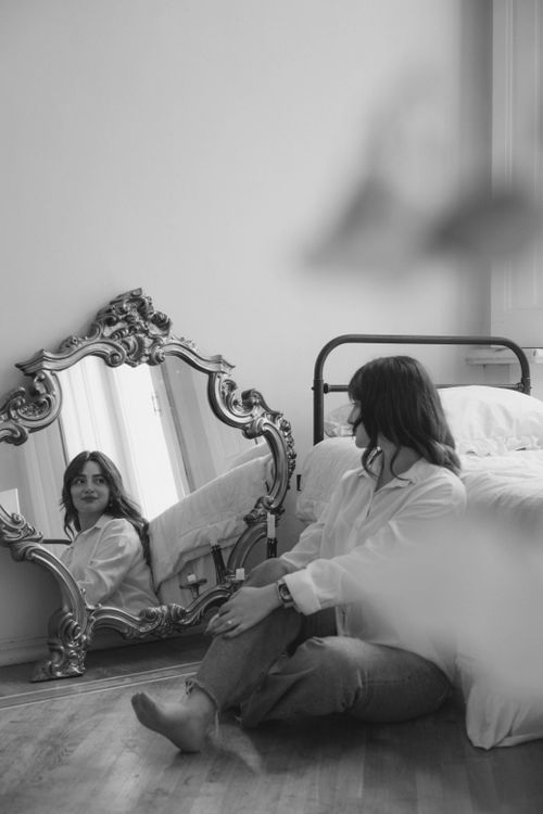 Free A woman sits by a vintage mirror in a cozy, elegant bedroom, reflecting a serene atmosphere. Stock Photo