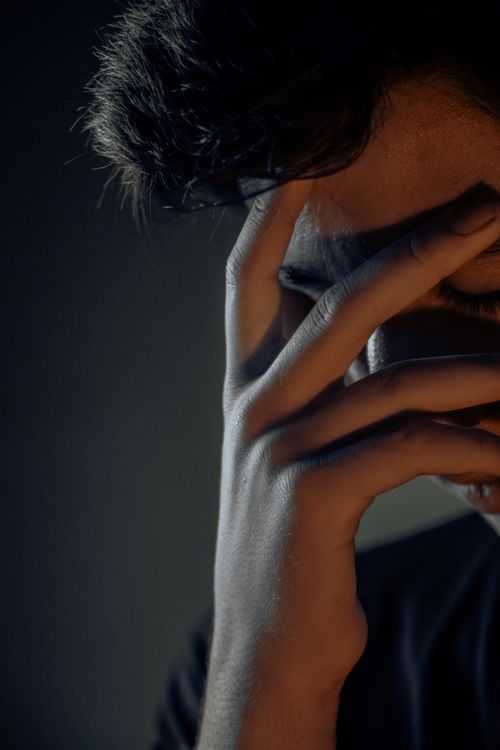Free Close-up of a young man with hand on face, expressing deep emotions in low light. Stock Photo