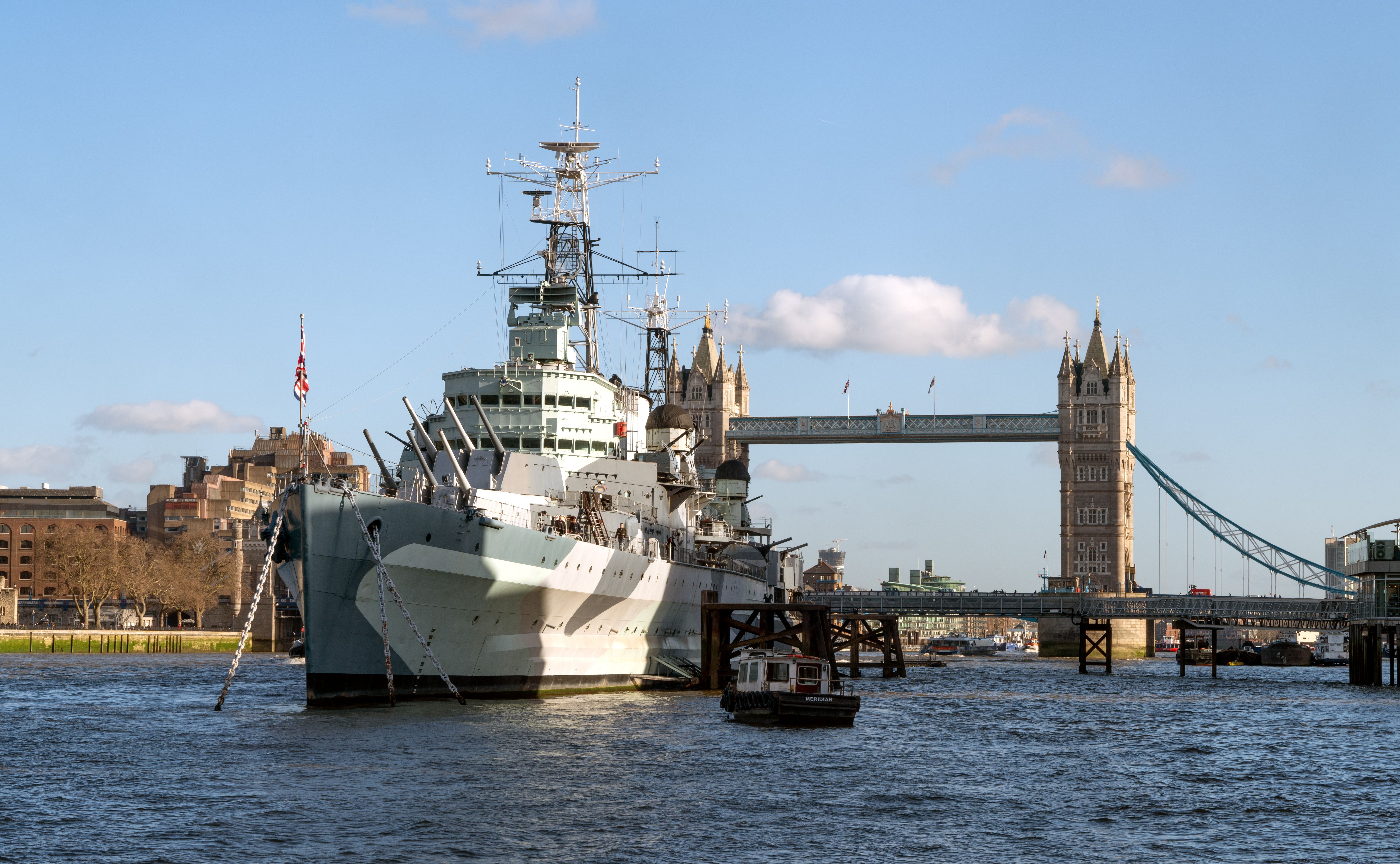 HMS Belfast moored on River Thames with iconic Tower Bridge in London.