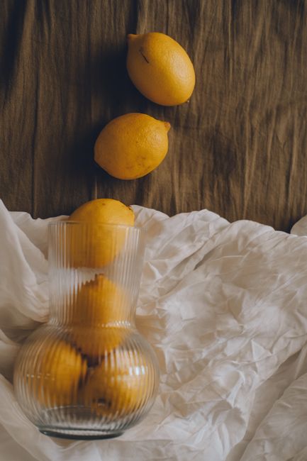 Artistic still life featuring lemons in a glass vase on a textile backdrop.