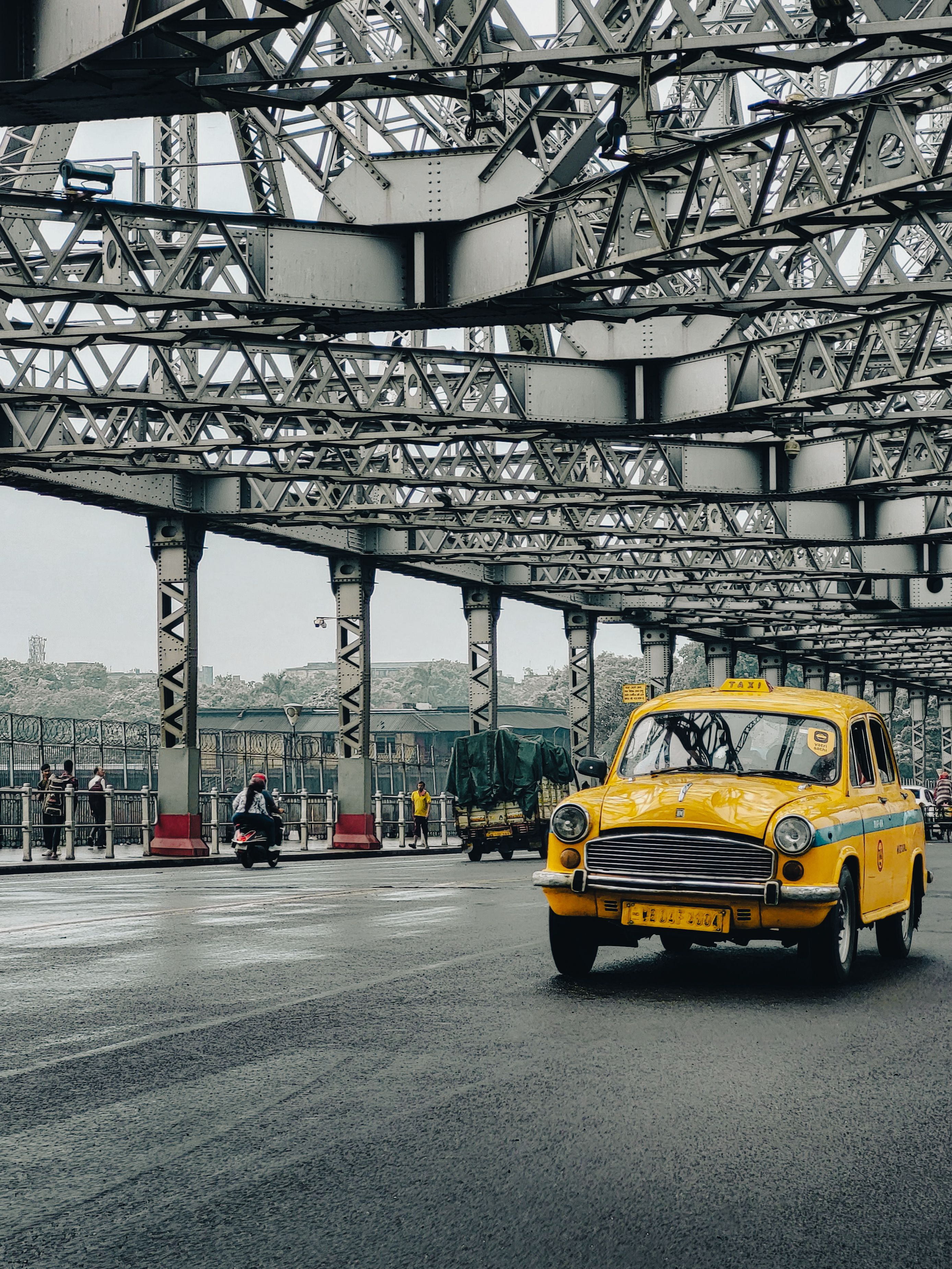 Classic yellow taxi drives on the historic Howrah Bridge in Kolkata, India.
