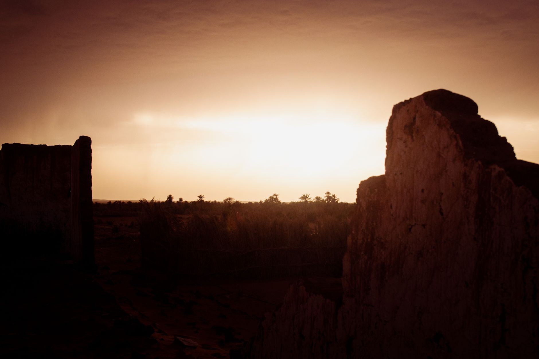 Silhouette of ancient ruins against a vibrant desert sunset, creating a dramatic landscape.