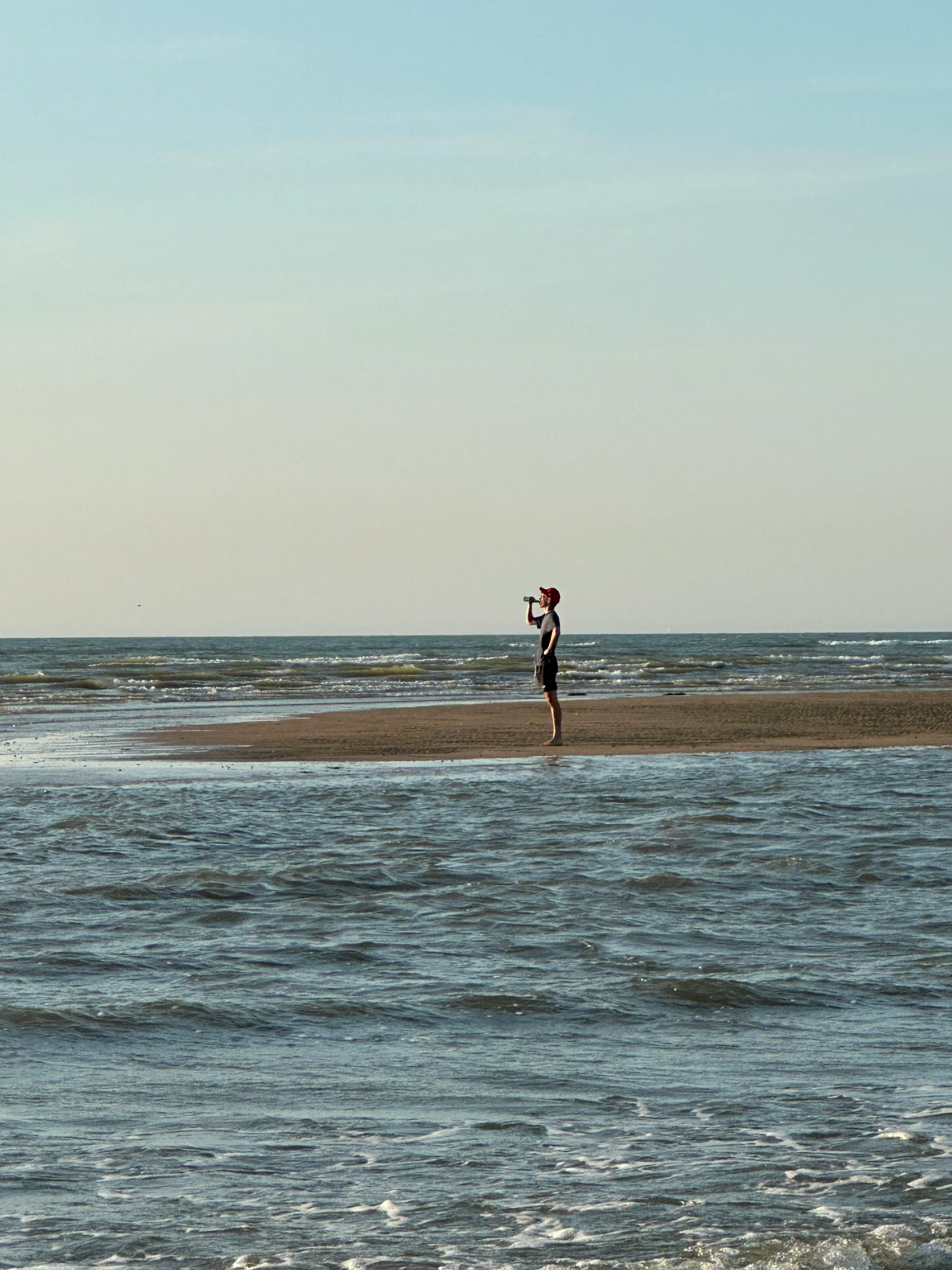 A person stands on a tranquil beach in Cabourg, Normandy, seemingly enjoying a drink.