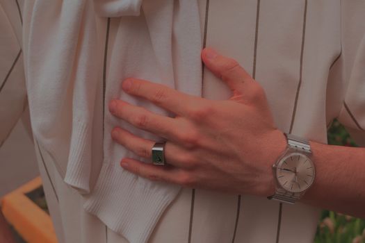 Close-up of a hand wearing a wristwatch and ring, holding a white garment.