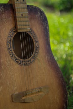 A close-up of a vintage acoustic guitar outdoors, showcasing its wooden body and intricate soundhole design.