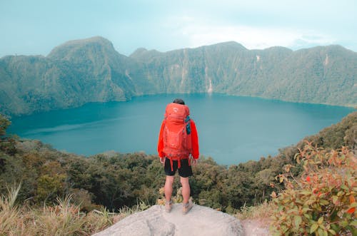 Back View of a Man with a Backpack Standing on a Hill and Looking at the Lake in the Valley 