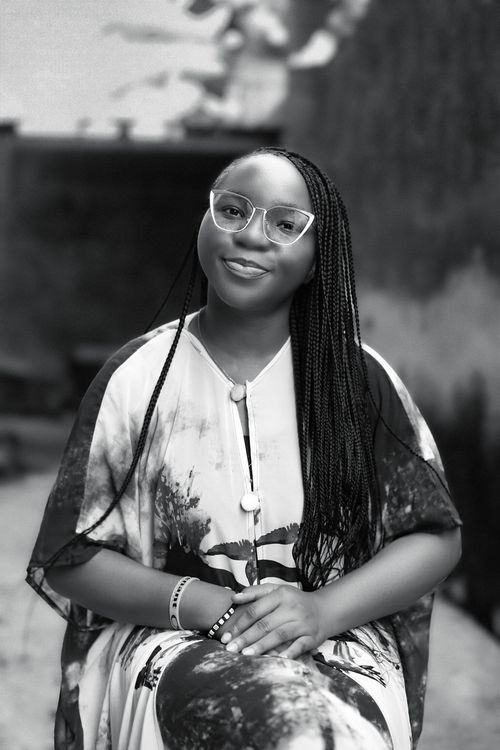Free Stylish black woman smiling in eyeglasses, sitting outdoors in black and white portrait. Stock Photo