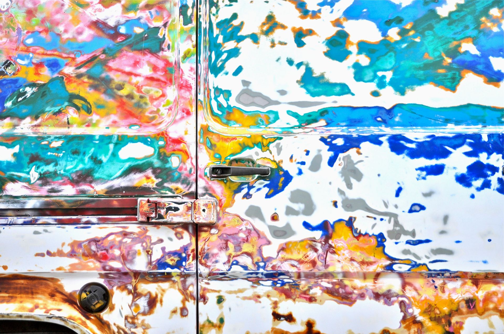 Close-up view of a car door showcasing colorful, vibrant paint patterns and textures in an abstract style.