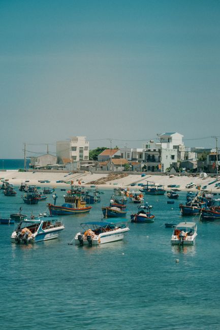 Discover a charming coastal town with boats anchored in a serene bay under a clear sky.