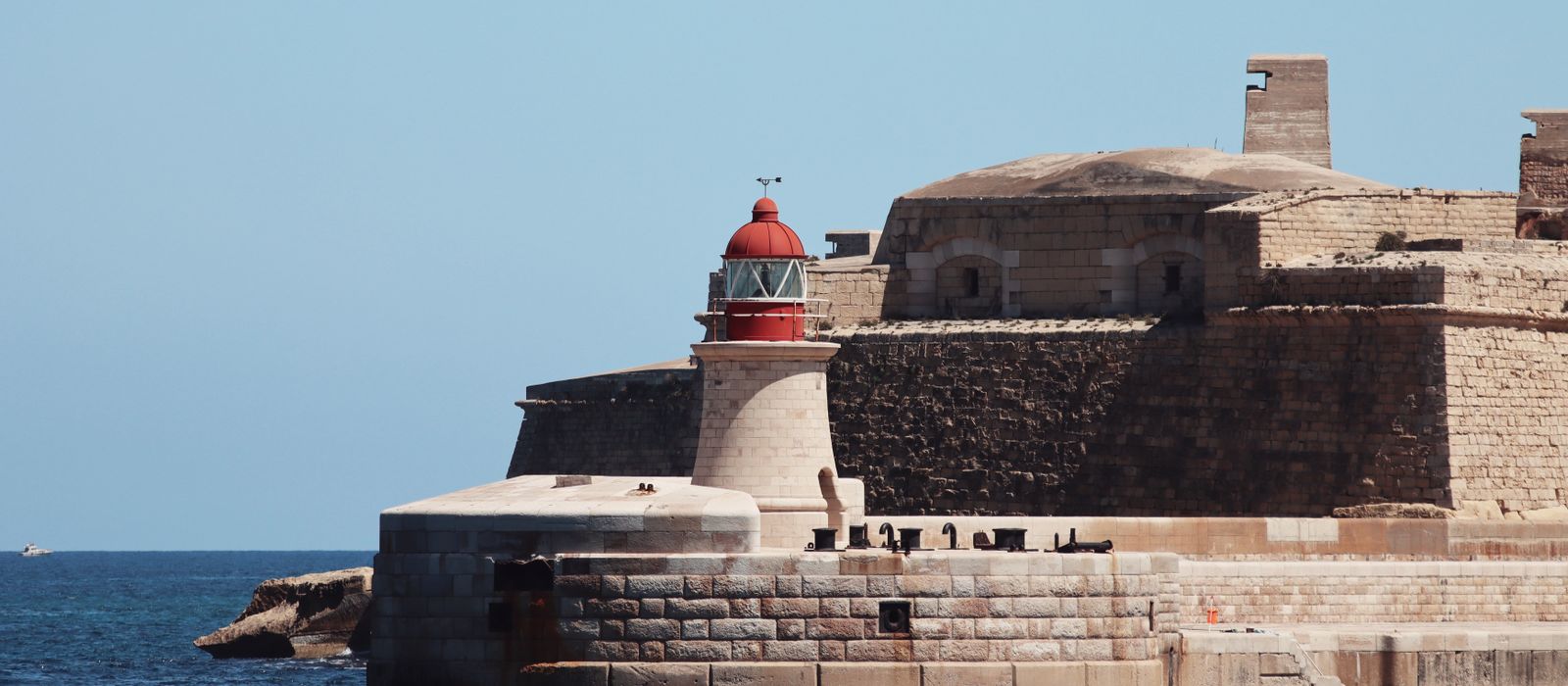 A striking lighthouse stands by ancient fortifications on the seaside at Valletta, Malta. — flights from Rome to Malta