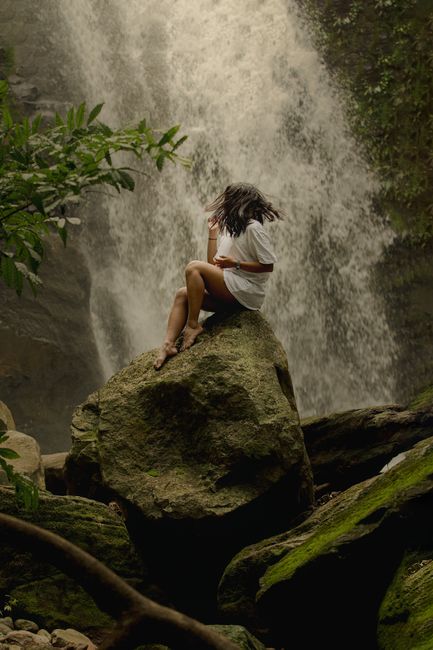 A serene moment captured with a woman sitting atop a rock near a waterfall in Panama's tropical jungle.