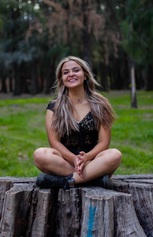 Pretty Young Woman Smiling and Sitting on a Trunk in a Park