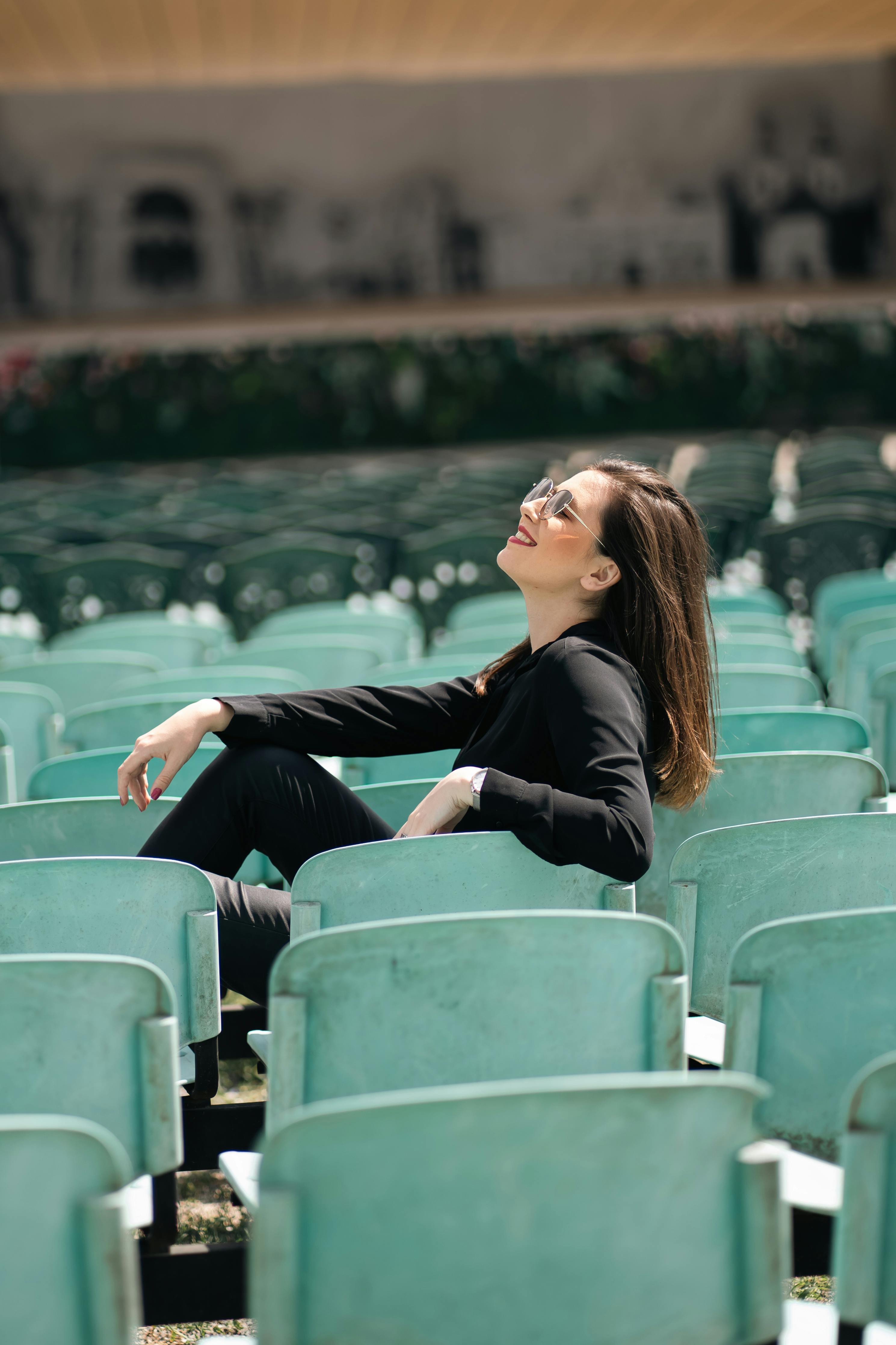 Free A woman with sunglasses lounges among amphitheater seats, enjoying a sunny day. Stock Photo