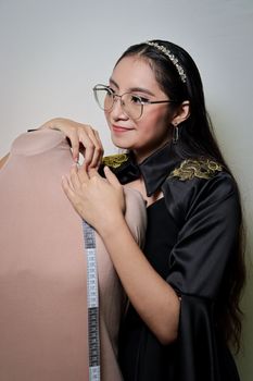 Young fashion designer smiling while working with mannequin in studio.