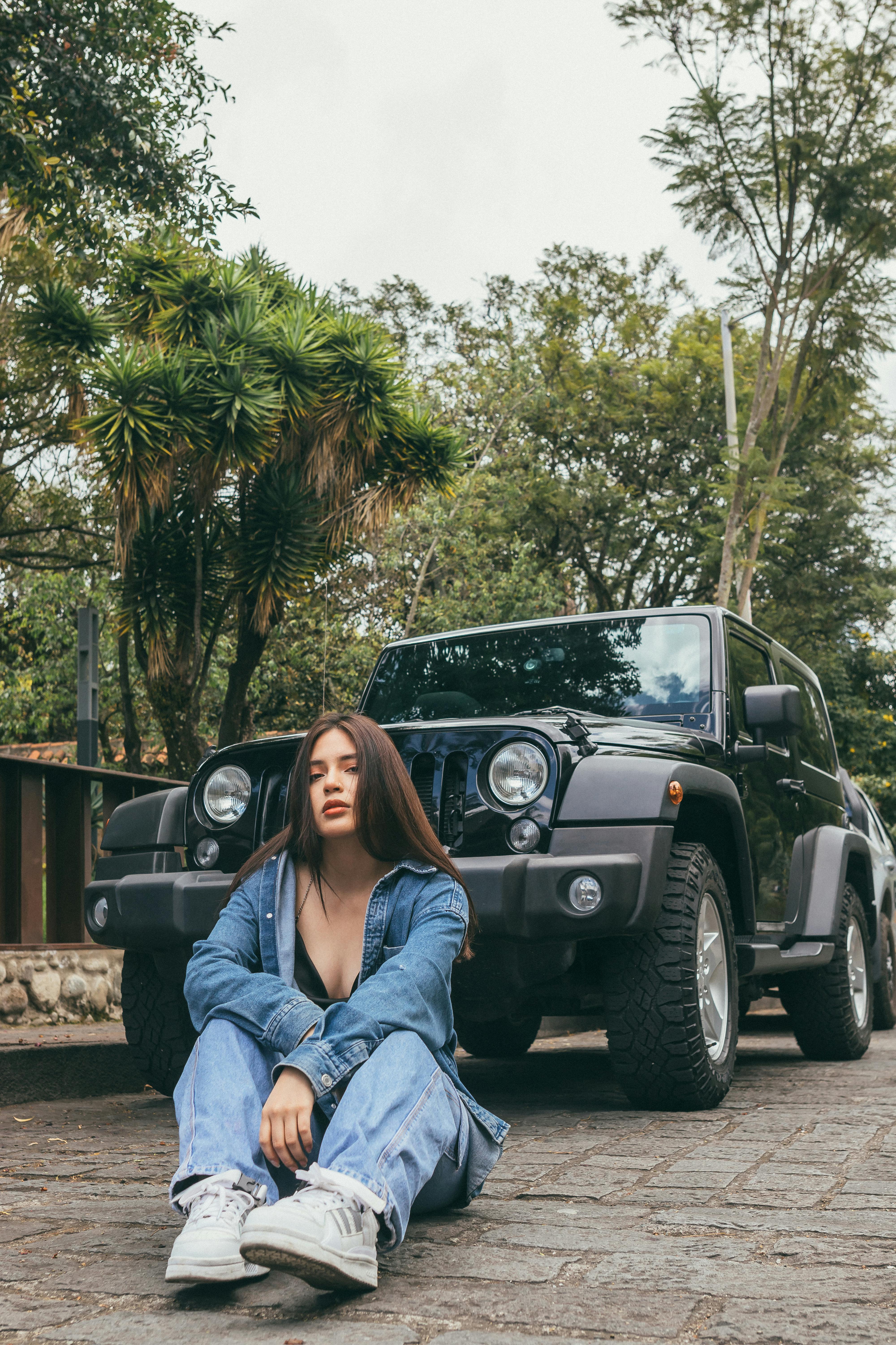 Young Woman Sitting on the Pavement in front of a Jeep · Free Stock Photo