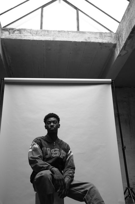 Black and white portrait of a man in a studio setting wearing a USA jacket, showcasing fashion photography.