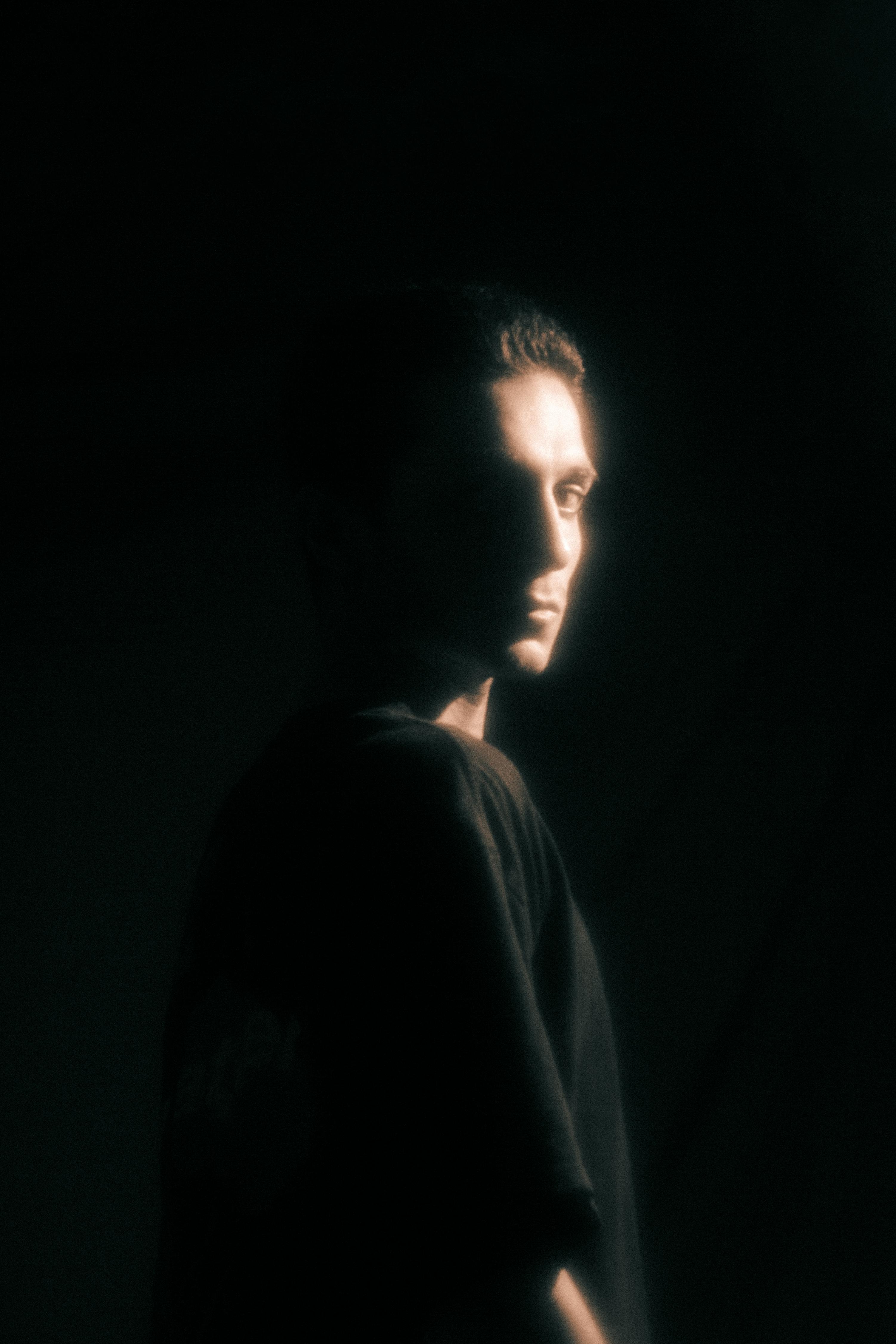 Artistic portrait of a man standing in soft dramatic light against a dark background.