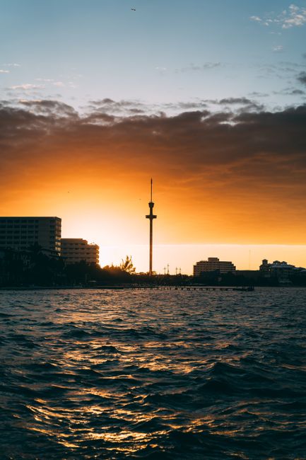 Captivating sunset over urban skyline with ocean foreground, highlighting silhouetted tower.
