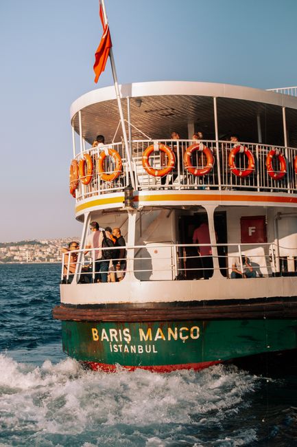 A ferry in Istanbul navigates the Bosphorus with visible life belts and passengers enjoying the ride.