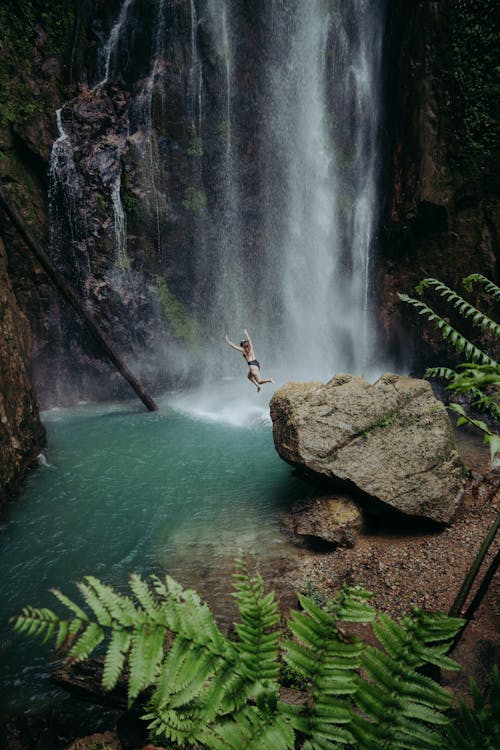 Woman Jumping from Rock near Waterfall