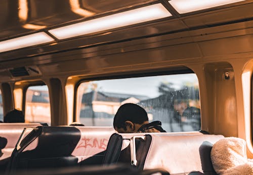 Free A man sitting inside a sunlit bus, gazing out of the window with warm lighting. Stock Photo
